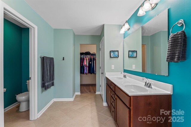 full bathroom featuring double vanity, a sink, toilet, and baseboards