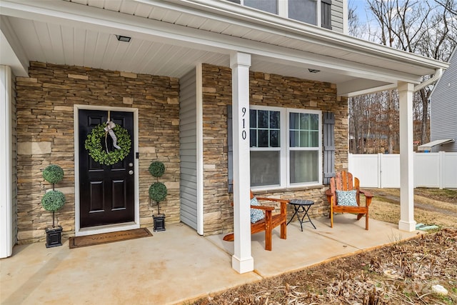 doorway to property featuring stone siding, fence, and covered porch