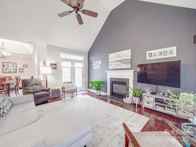 living area with baseboards, a fireplace with flush hearth, dark wood-type flooring, high vaulted ceiling, and ceiling fan with notable chandelier