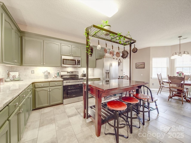 kitchen with stainless steel appliances, decorative light fixtures, green cabinetry, and tasteful backsplash