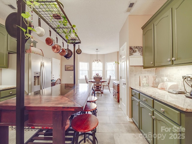 kitchen featuring tasteful backsplash, stainless steel fridge with ice dispenser, green cabinets, light stone countertops, and pendant lighting