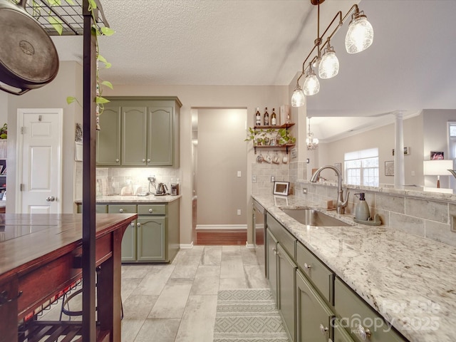 kitchen featuring a sink, decorative backsplash, light stone countertops, decorative light fixtures, and green cabinetry