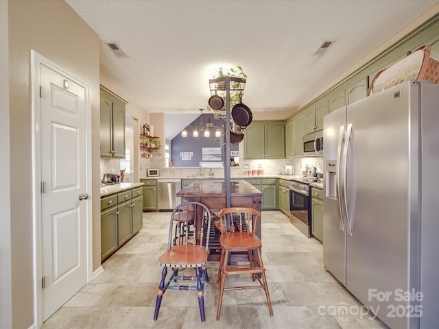 kitchen with appliances with stainless steel finishes, light countertops, green cabinetry, and decorative backsplash