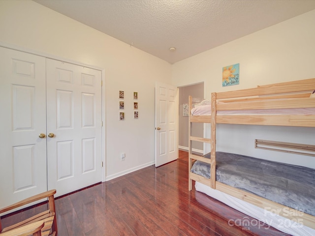 bedroom featuring a textured ceiling, dark wood-type flooring, a closet, and baseboards