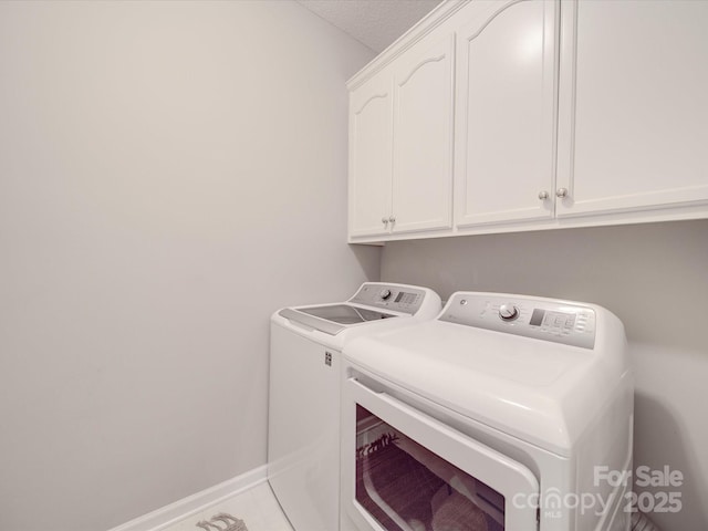 washroom with washing machine and dryer, cabinet space, a textured ceiling, and baseboards