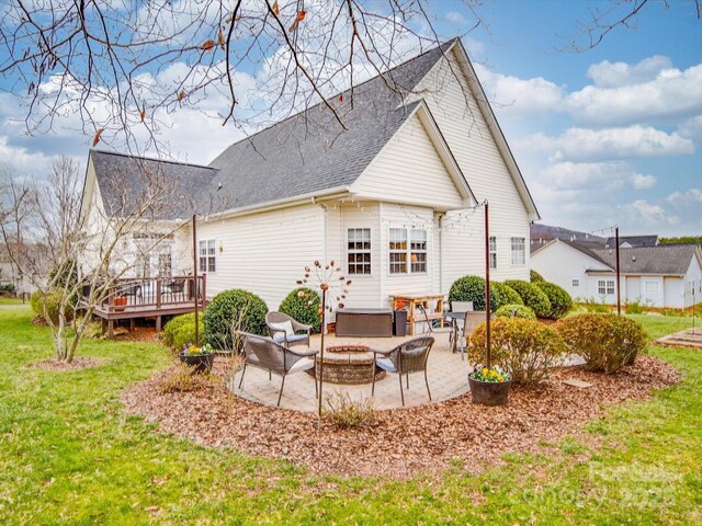 back of property with a shingled roof, a lawn, a patio area, a deck, and a fire pit