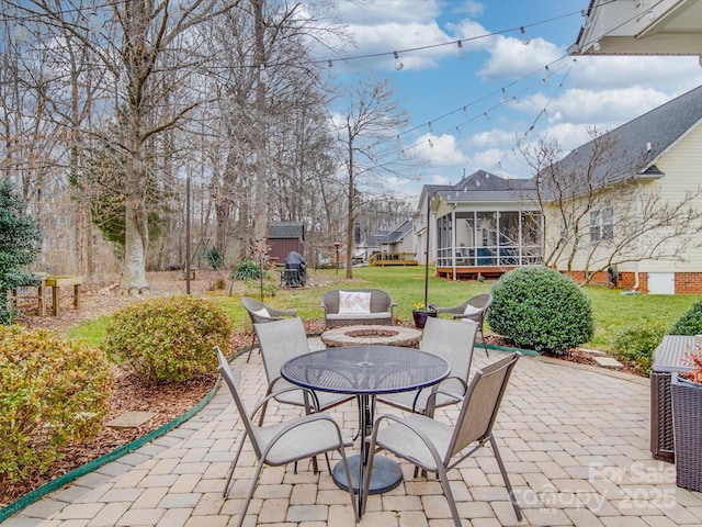 view of patio with outdoor dining space, a sunroom, and an outdoor fire pit