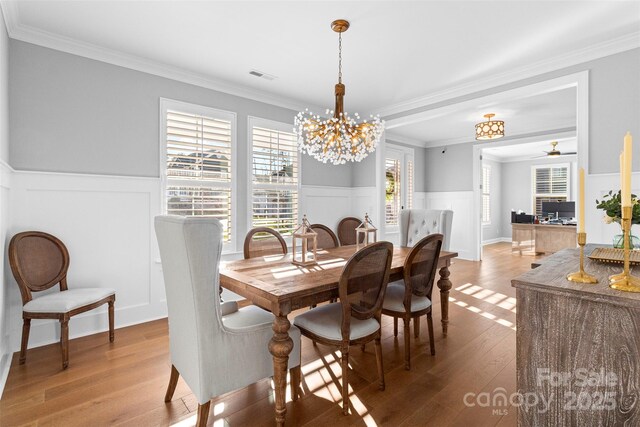 dining room featuring ornamental molding, light wood-type flooring, a wainscoted wall, and visible vents