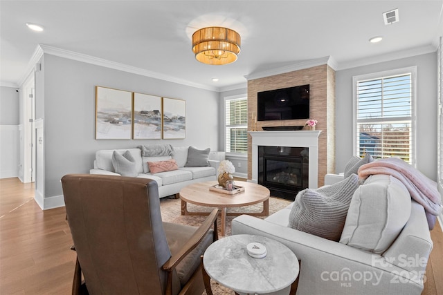 living area with baseboards, visible vents, wood finished floors, crown molding, and a fireplace