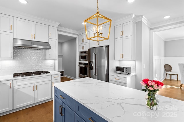 kitchen with decorative light fixtures, stainless steel appliances, ornamental molding, white cabinets, and under cabinet range hood