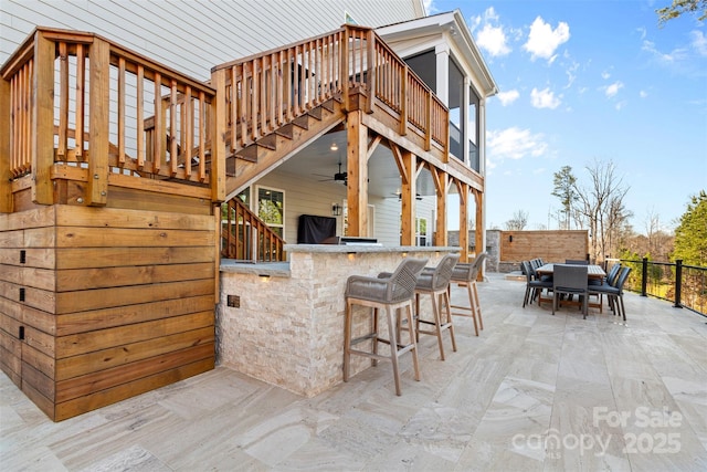 view of patio featuring outdoor dry bar, outdoor dining space, stairs, and a ceiling fan