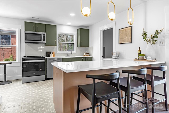 5825 Ruth Dr, Charlotte, NC 28215 - kitchen featuring decorative backsplash, appliances with stainless steel finishes, green cabinetry, a peninsula, and a kitchen breakfast bar