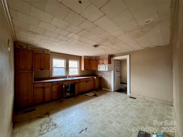 kitchen featuring white microwave, brown cabinets, hanging light fixtures, light countertops, and a sink