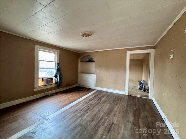 unfurnished room featuring baseboards, a textured wall, wood finished floors, and crown molding