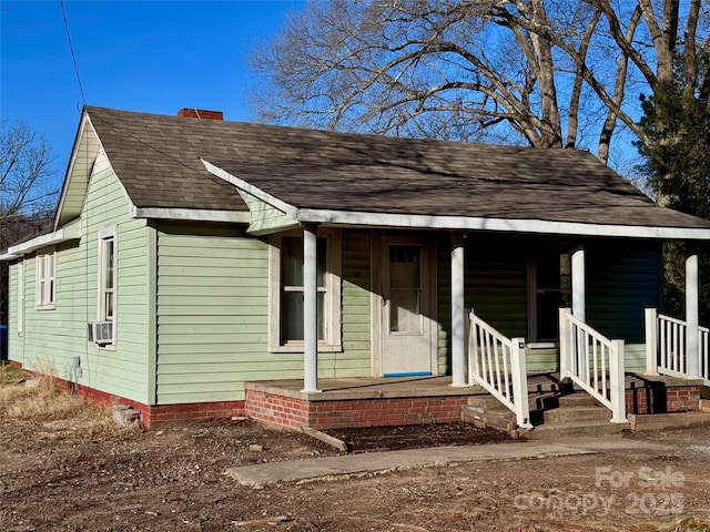 view of front of property featuring covered porch, a chimney, cooling unit, and roof with shingles