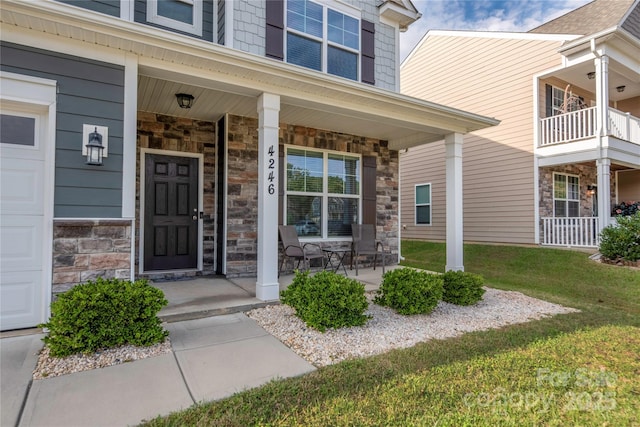 view of exterior entry with an attached garage, stone siding, a yard, and covered porch