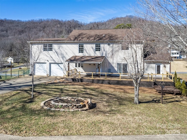 back of house with a fire pit, concrete driveway, a deck, and a lawn