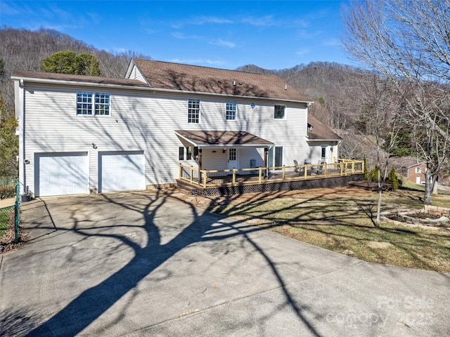 rear view of property with driveway, an attached garage, a lawn, and a deck with mountain view