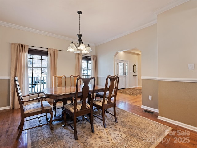 dining room featuring arched walkways, a notable chandelier, wood finished floors, visible vents, and ornamental molding