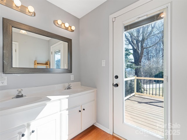 bathroom with wood finished floors, a sink, baseboards, and double vanity