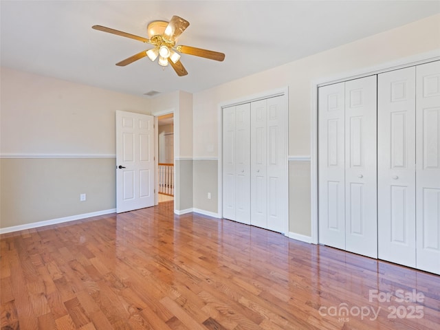 unfurnished bedroom with visible vents, baseboards, two closets, and wood finished floors