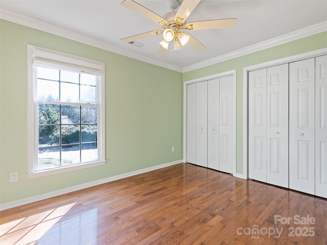 unfurnished bedroom with crown molding, multiple closets, and wood finished floors