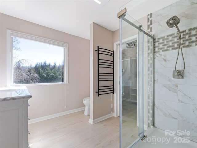 full bathroom with toilet, a stall shower, baseboards, and vanity