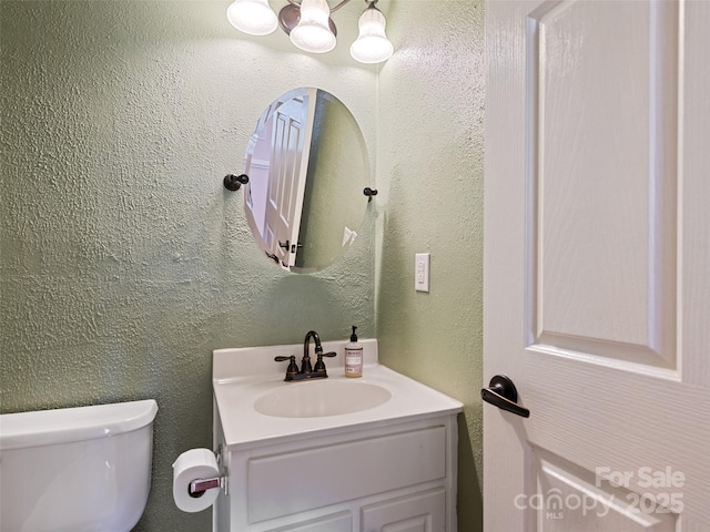 bathroom featuring toilet, vanity, and a textured wall