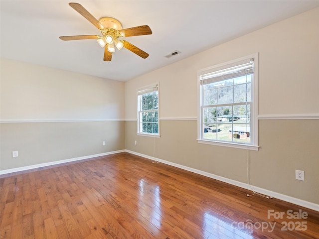 empty room with wood-type flooring, visible vents, ceiling fan, and baseboards