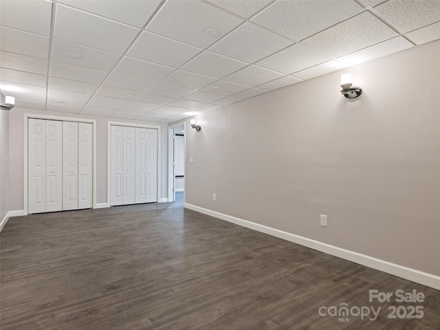 below grade area with a paneled ceiling, dark wood finished floors, and baseboards