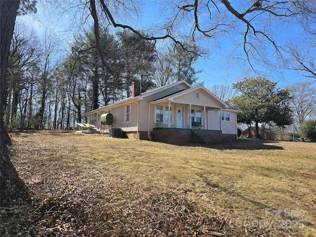 view of front of house with central air condition unit, covered porch, a chimney, and a front lawn