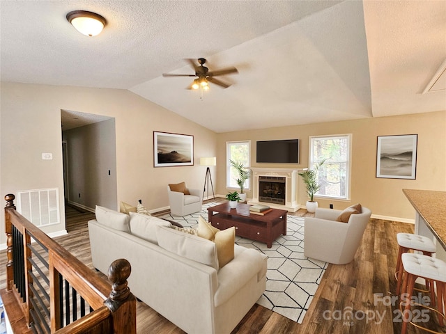 living area featuring a textured ceiling, a fireplace, wood finished floors, visible vents, and vaulted ceiling