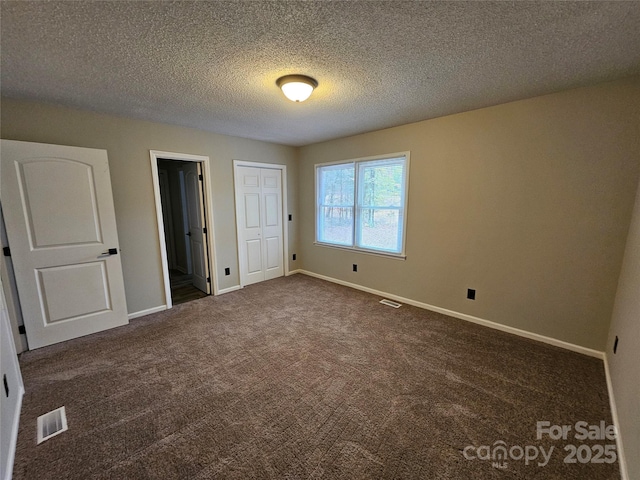 unfurnished bedroom with dark colored carpet, visible vents, a textured ceiling, and baseboards