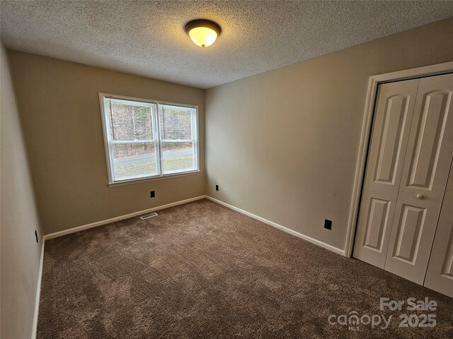 unfurnished bedroom featuring carpet, a closet, visible vents, a textured ceiling, and baseboards