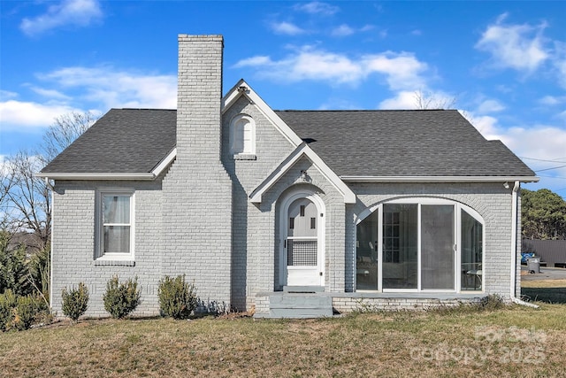 view of front of house featuring a shingled roof, a front lawn, brick siding, and a chimney