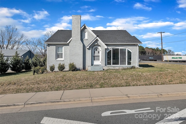 view of front of home with a shingled roof, a front lawn, brick siding, and a chimney