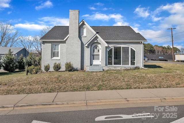 view of front of property featuring a front yard, brick siding, a chimney, and a shingled roof