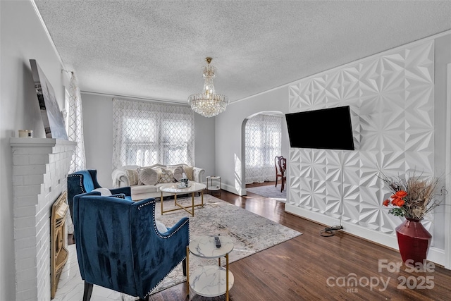 living area featuring wood finished floors, baseboards, a textured ceiling, a brick fireplace, and a notable chandelier