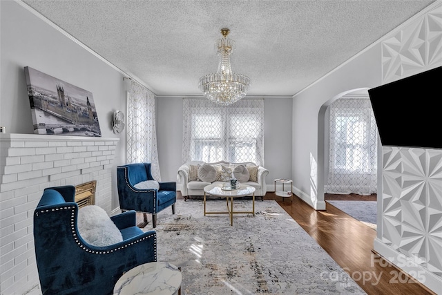 living area with ornamental molding, an inviting chandelier, wood finished floors, arched walkways, and a textured ceiling