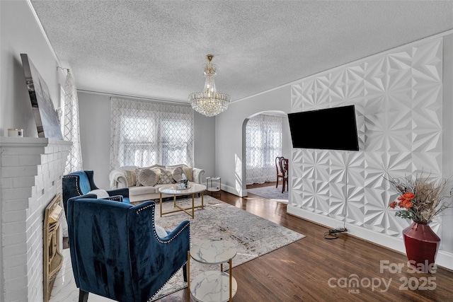 living area featuring a textured ceiling, wood finished floors, arched walkways, an inviting chandelier, and a brick fireplace