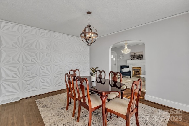 dining room with visible vents, wood finished floors, arched walkways, a fireplace, and baseboards