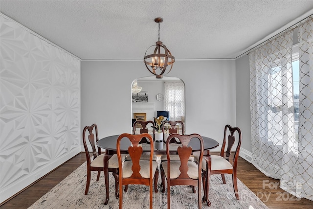 dining room featuring a notable chandelier, dark wood-type flooring, a textured ceiling, arched walkways, and a fireplace