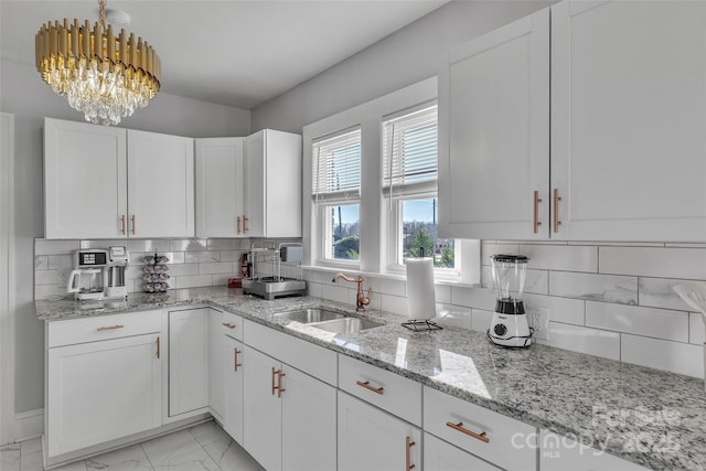 kitchen with a sink, marble finish floor, white cabinetry, a notable chandelier, and tasteful backsplash