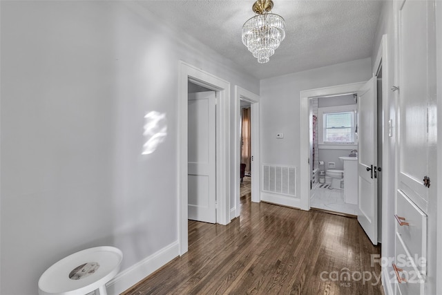 hall with visible vents, baseboards, wood finished floors, a notable chandelier, and a textured ceiling