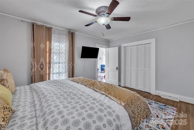 bedroom with wood finished floors, baseboards, visible vents, a closet, and a textured ceiling