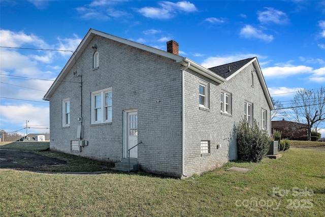 view of home's exterior with brick siding, a lawn, entry steps, and a chimney