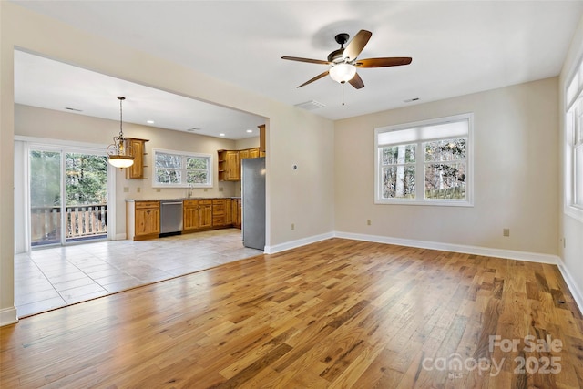 unfurnished living room with light wood finished floors, visible vents, a ceiling fan, a sink, and baseboards