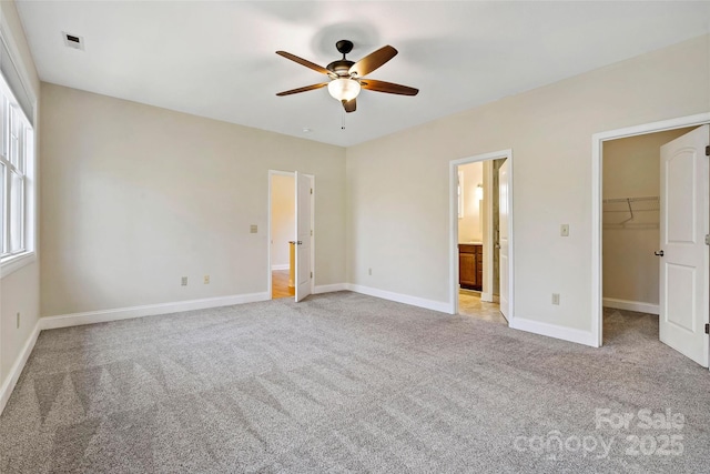 unfurnished bedroom with a walk in closet, visible vents, light carpet, connected bathroom, and baseboards