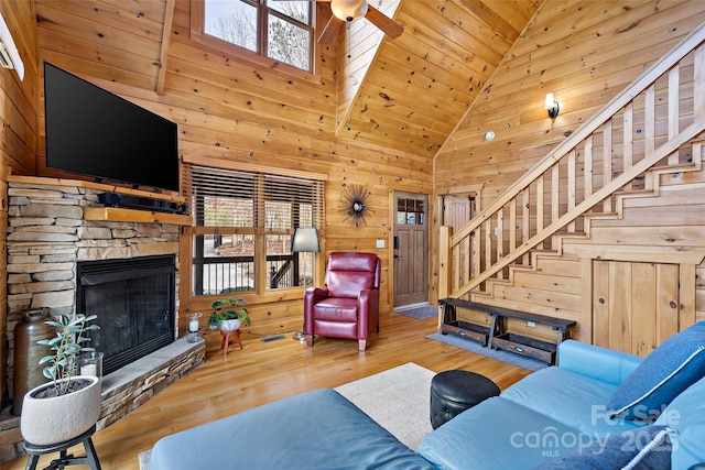 living room featuring wooden walls, a fireplace, wood finished floors, stairs, and vaulted ceiling