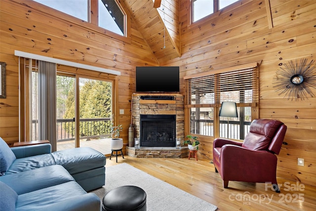 living room featuring high vaulted ceiling, wood walls, a fireplace, and wood finished floors